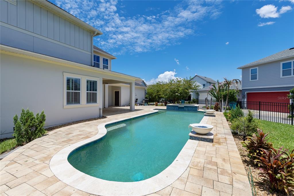 A backyard features a swimming pool with a spa, stone pavers, and a covered patio — 9051 SPERRY STREET, ORLANDO, FL