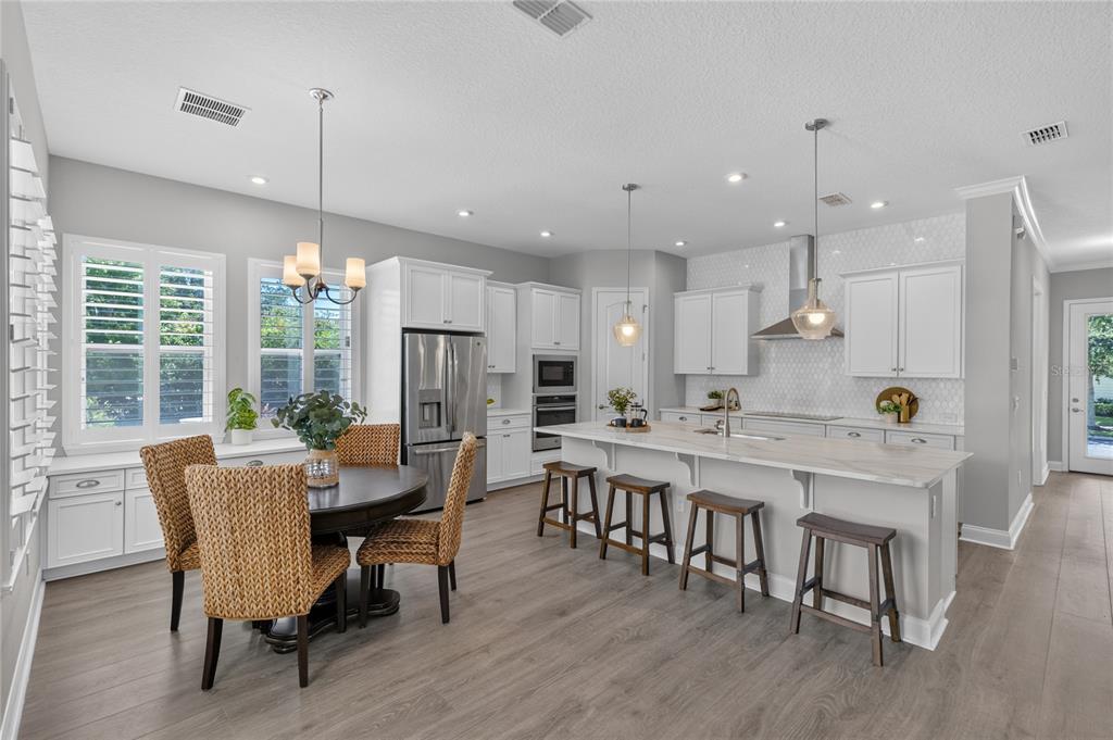A bright kitchen features white cabinetry, a large island with bar seating, and dining area — 9051 SPERRY STREET, ORLANDO, FL