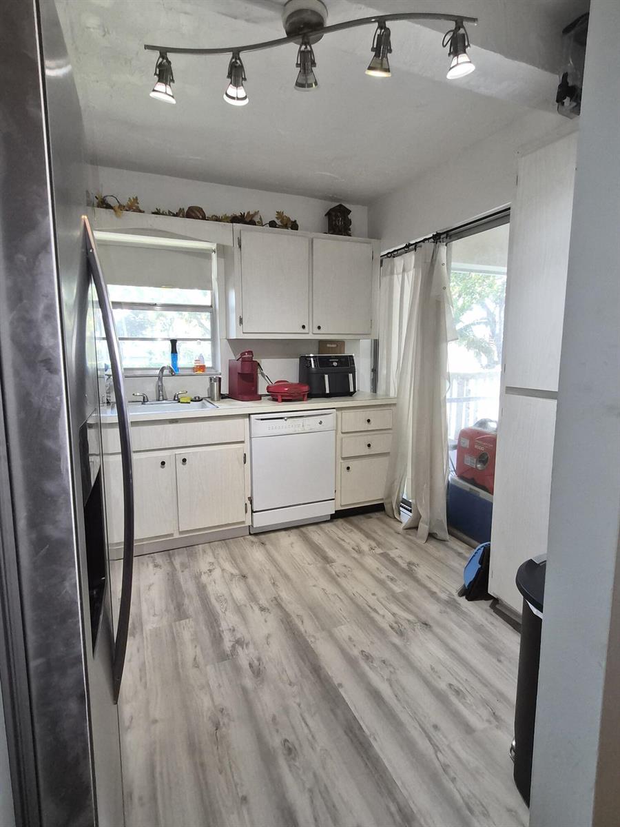 A kitchen features white cabinets, light wood-look flooring, a dishwasher, and a track lighting fixture — 100 Royal Palm Way # 2040, Boca Raton FL 33432, BOCA RATON, FL