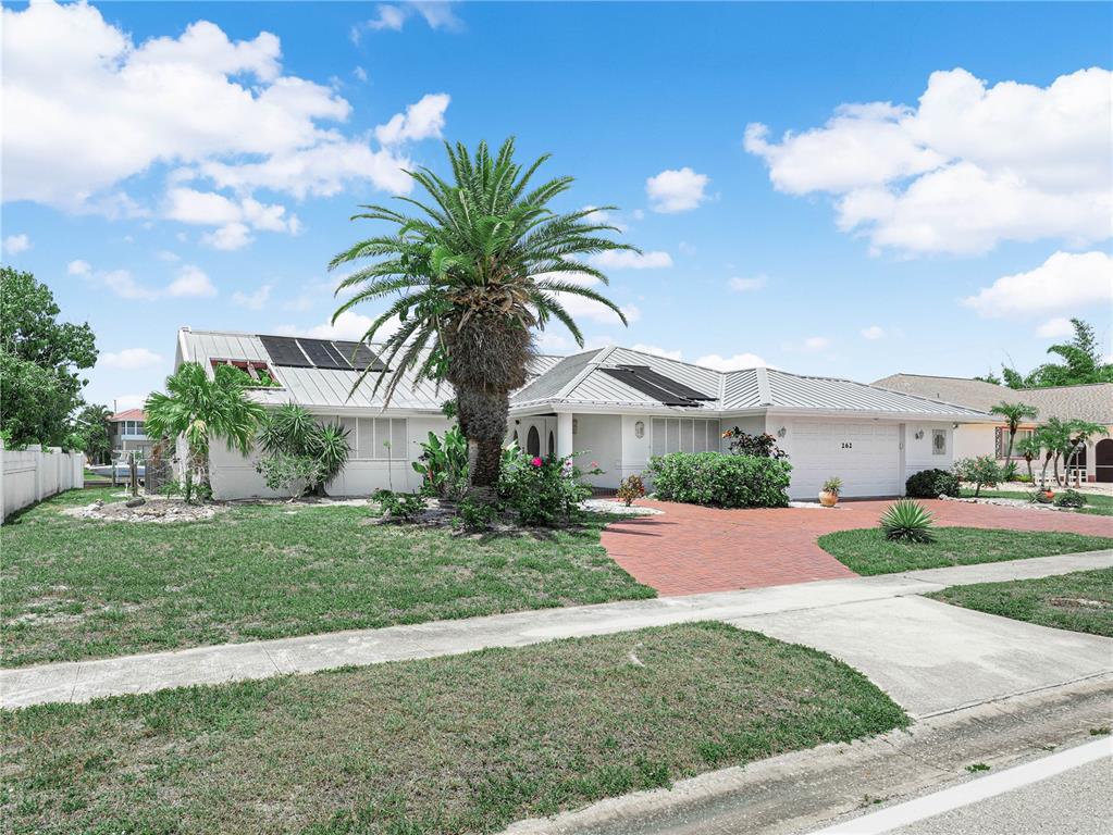 A single-story house with a metal roof, palm tree, and brick driveway under a blue sky — 262 GEORGE ROAD SE, PORT CHARLOTTE, FL