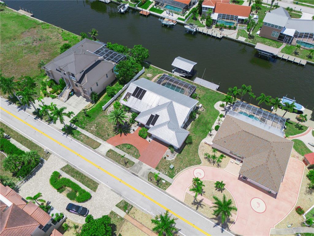 An aerial view shows three waterfront houses with pools along a canal and a road — 262 GEORGE ROAD SE, PORT CHARLOTTE, FL
