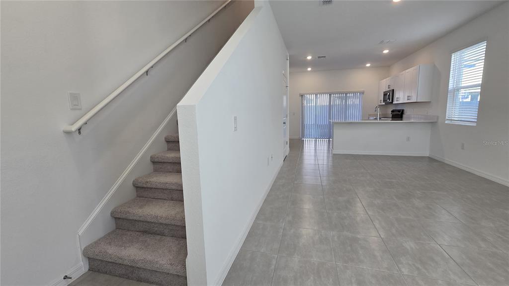 A carpeted staircase leads to an upper floor next to an open-concept kitchen and living area — 2970 SKYLINE LOOP, POINCIANA, FL