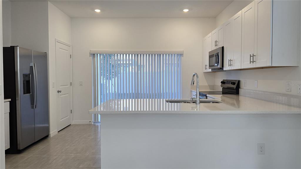 A kitchen features white cabinets, stainless steel appliances, and a quartz-topped island with a sink — 2970 SKYLINE LOOP, POINCIANA, FL