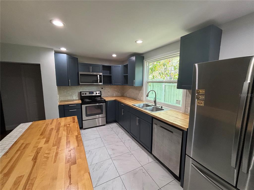 A kitchen features dark blue cabinets, butcher block countertops, stainless steel appliances, and tiled flooring — 1319 S MICHIGAN AVENUE, CLEARWATER, FL