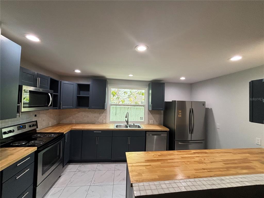 A kitchen features dark blue cabinets, butcher block countertops, stainless steel appliances, and tile flooring — 1319 S MICHIGAN AVENUE, CLEARWATER, FL