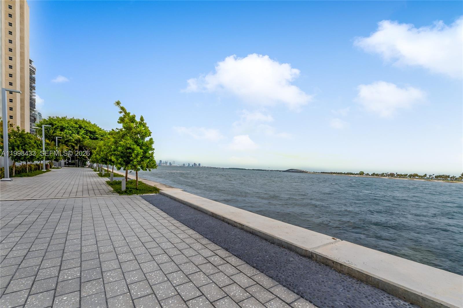 A paved waterfront walkway runs alongside a body of water with a distant city skyline — 150 SE 25th Rd # 12B, Miami FL 33129, MIAMI, FL