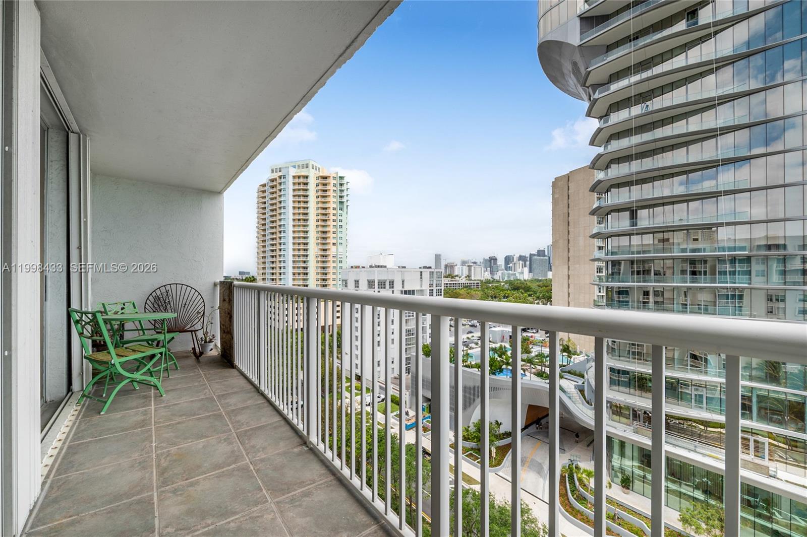 A balcony with green metal furniture overlooks a city skyline and modern high-rise buildings — 150 SE 25th Rd # 12B, Miami FL 33129, MIAMI, FL