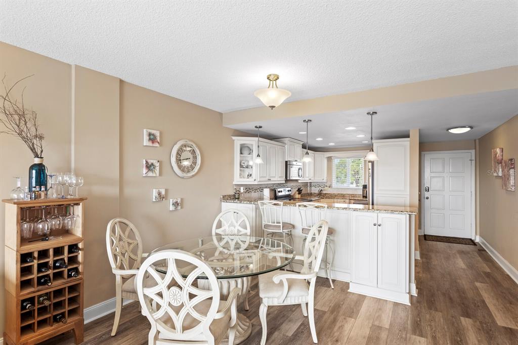 A dining area with a glass table and wine rack opens into a white kitchen — 1200 N SHORE DRIVE NE UNIT 407, ST PETERSBURG, FL
