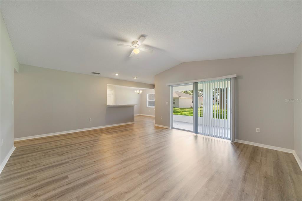 A living room with light wood-look flooring, a ceiling fan, and sliding glass patio doors — 437 JAY COURT, POINCIANA, FL