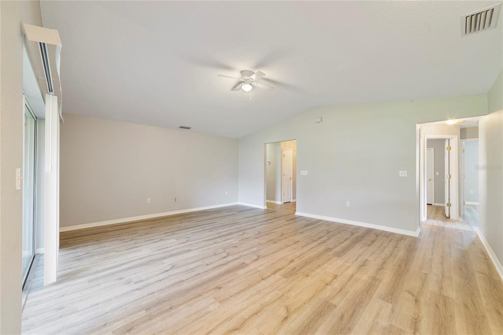 An empty living room features light wood-look flooring, neutral walls, and a ceiling fan — 437 JAY COURT, POINCIANA, FL