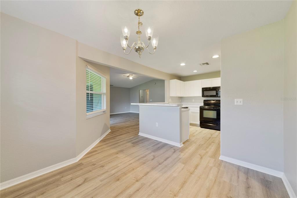 A dining area with a chandelier opens to a kitchen featuring white cabinets and appliances — 437 JAY COURT, POINCIANA, FL