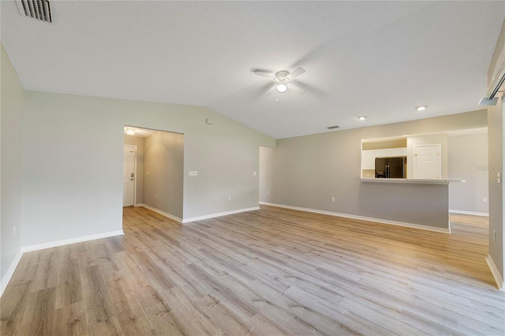 An open-concept living room features light wood-look flooring, a ceiling fan, and a kitchen pass-through — 437 JAY COURT, POINCIANA, FL