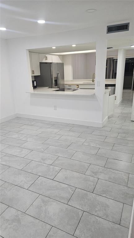 A kitchen with white cabinets and a breakfast bar overlooks a room with gray tile — 2500 21ST STREET NW UNIT 15, WINTER HAVEN, FL