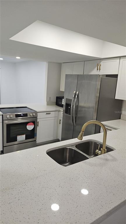 A kitchen features white cabinets, stainless steel appliances, and a quartz countertop with a sink — 2500 21ST STREET NW UNIT 15, WINTER HAVEN, FL