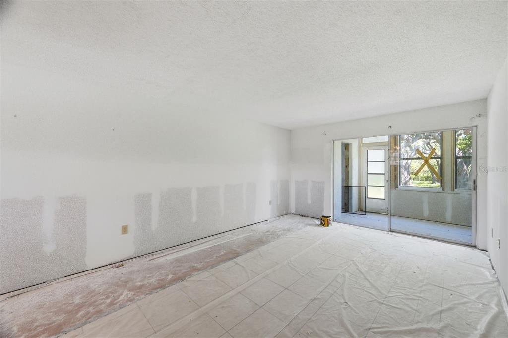 An unfinished room with white walls, exposed subfloor, and a sliding glass door to a porch — 4829 ONYX LANE UNIT 102, NEW PORT RICHEY, FL