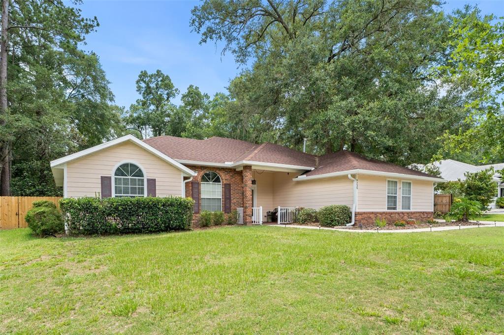A single-story house with beige siding, brick accents, and a covered entryway sits on grass — 9239 NW 16TH PLACE, GAINESVILLE, FL