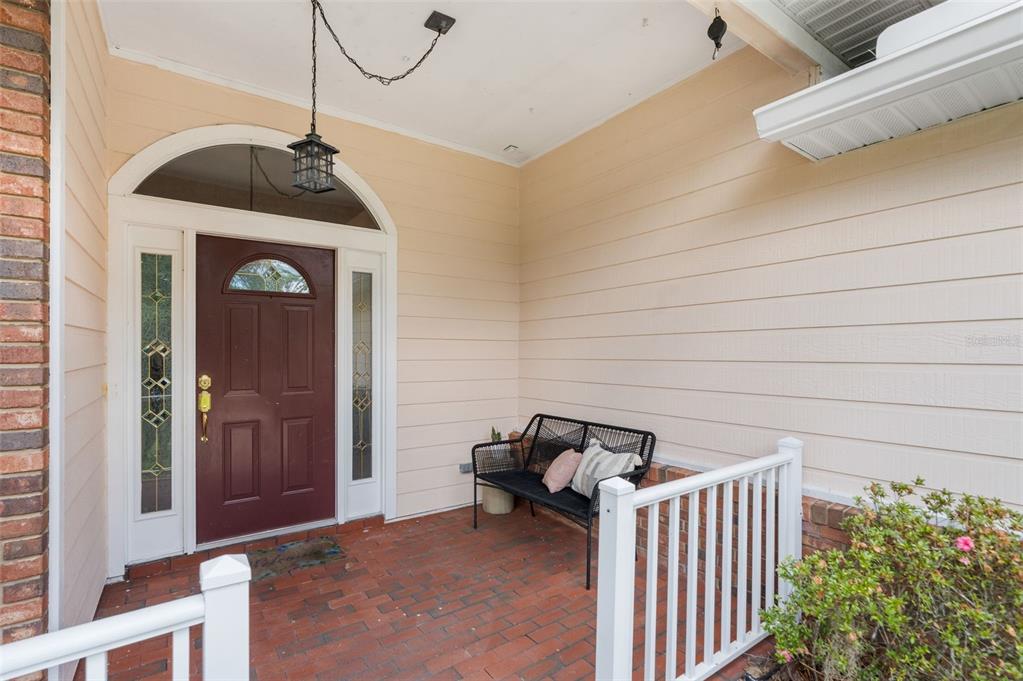 A covered brick porch features a dark red front door, a black bench, and railings — 9239 NW 16TH PLACE, GAINESVILLE, FL