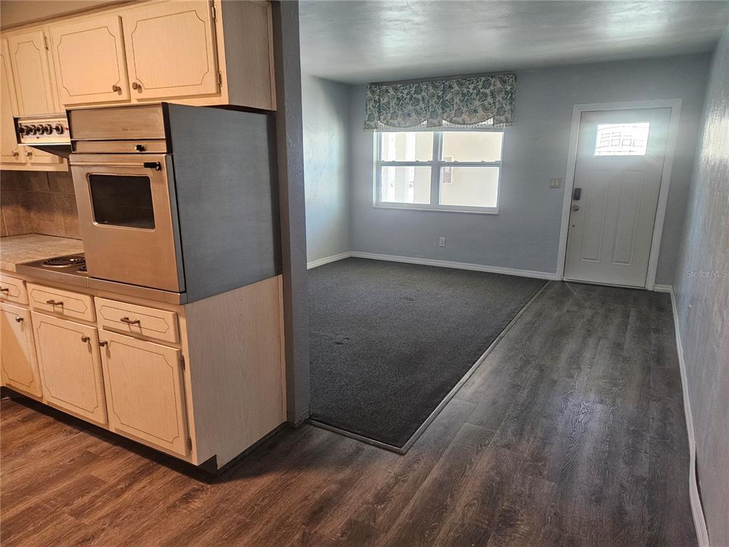 A kitchen with light wood cabinets and a wall oven opens into a carpeted room — 4565 DUHME ROAD UNIT 207, ST PETERSBURG, FL