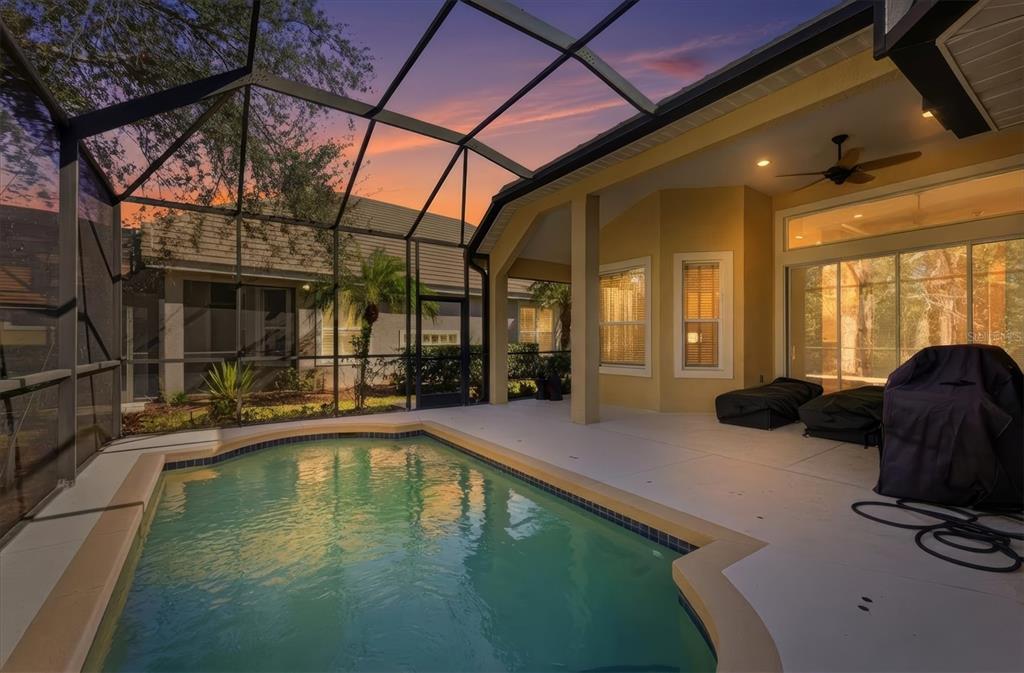 A screened-in patio features a swimming pool, a covered seating area, and a sunset view — 7478 EDENMORE STREET, LAKEWOOD RANCH, FL