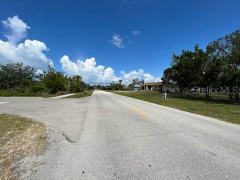 A paved road leads toward a residential house surrounded by trees under a blue sky — 310 W HENRY STREET, PUNTA GORDA, FL
