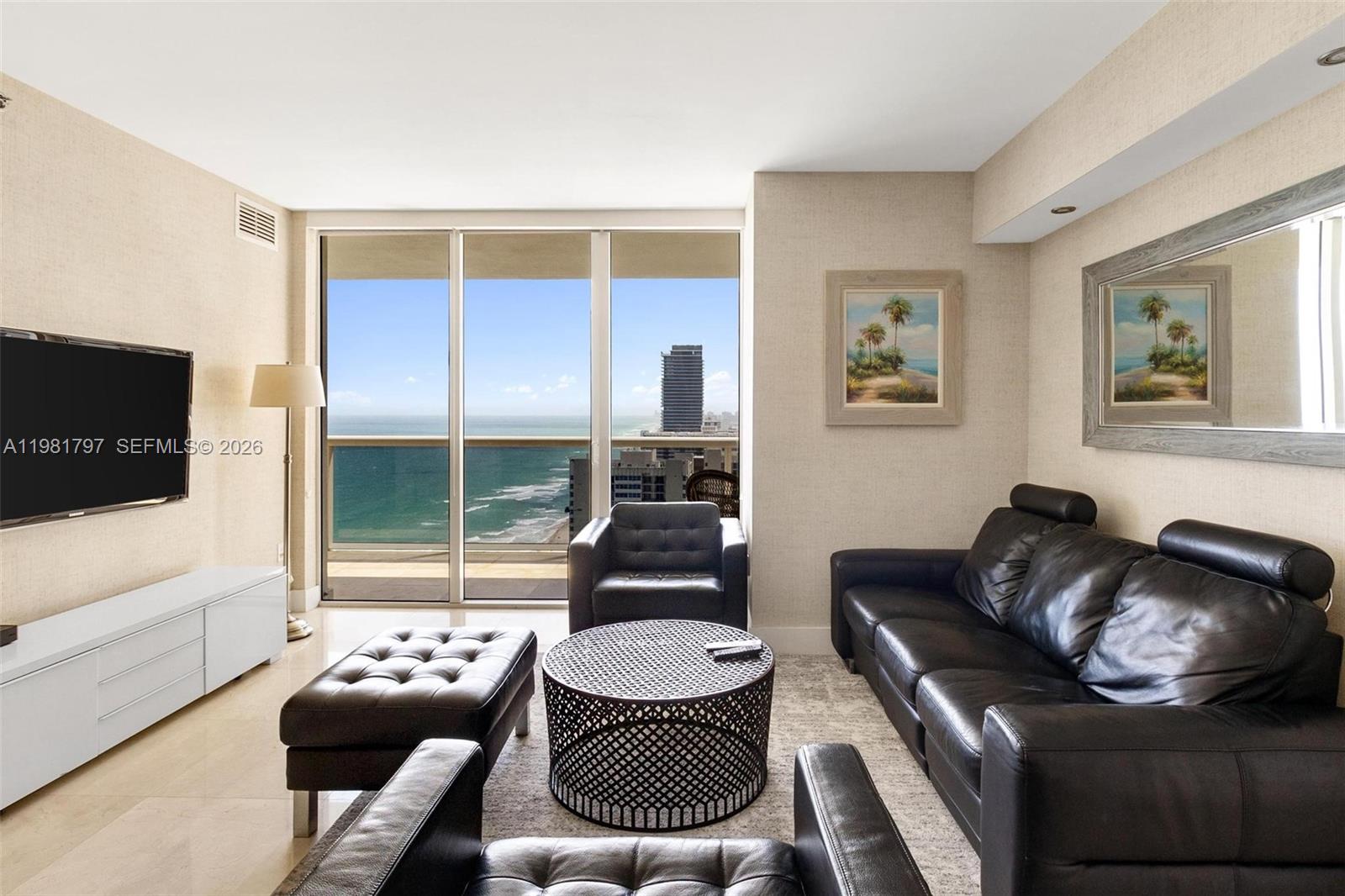 A living room features black leather furniture, a circular coffee table, and ocean views — 1830 S Ocean Dr # 2904, Hallandale Beach FL 33009, HALLANDALE BEACH, FL