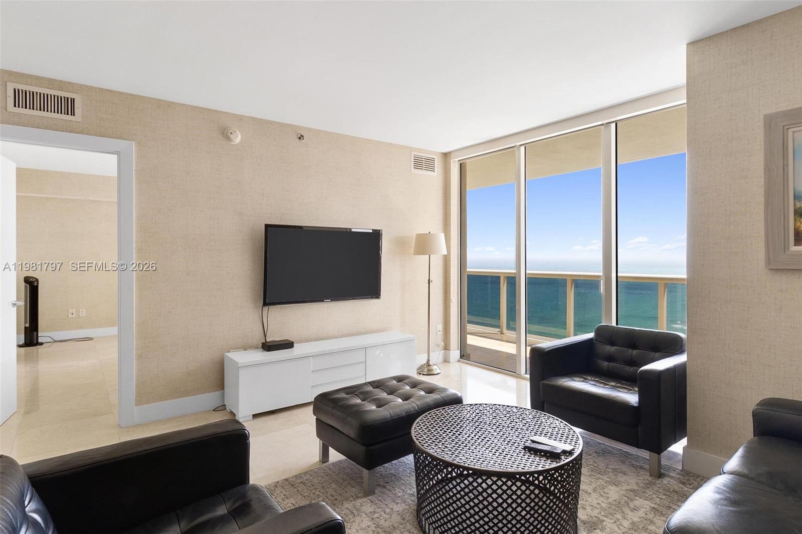 A living room features black leather furniture, a white media console, and a balcony view — 1830 S Ocean Dr # 2904, Hallandale Beach FL 33009, HALLANDALE BEACH, FL