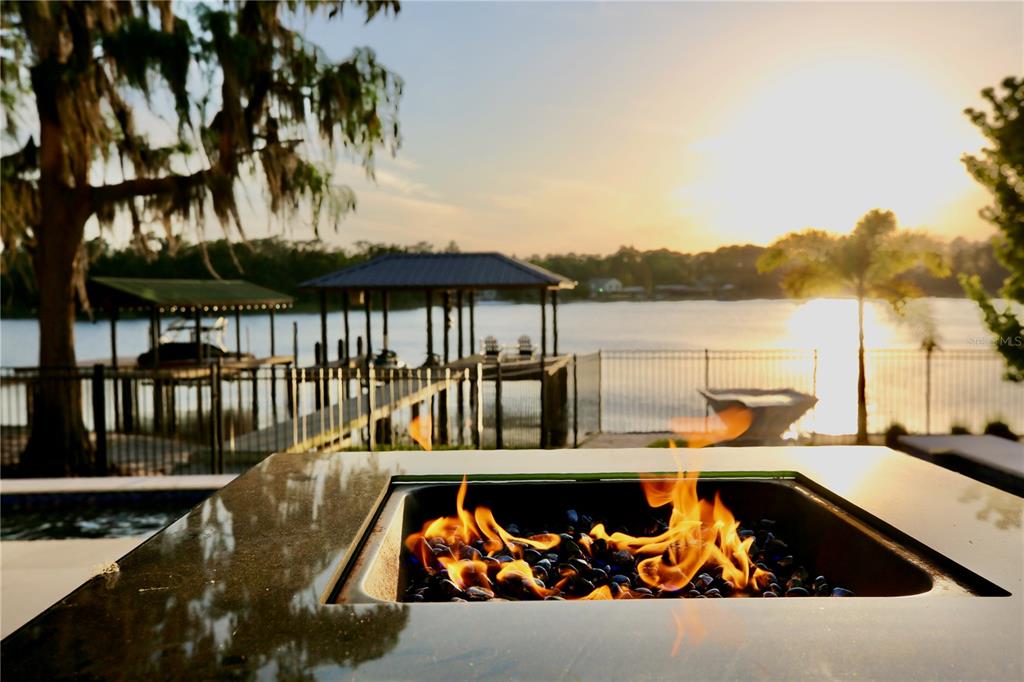 A fire pit with glass rocks overlooks a lake with boat docks at sunset — 17104 CRAWLEY ROAD, ODESSA, FL