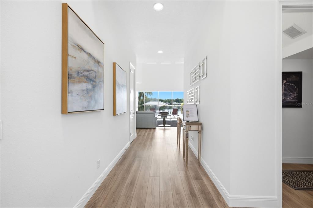 A bright hallway with light wood flooring leads to a living area overlooking a lake — 17104 CRAWLEY ROAD, ODESSA, FL