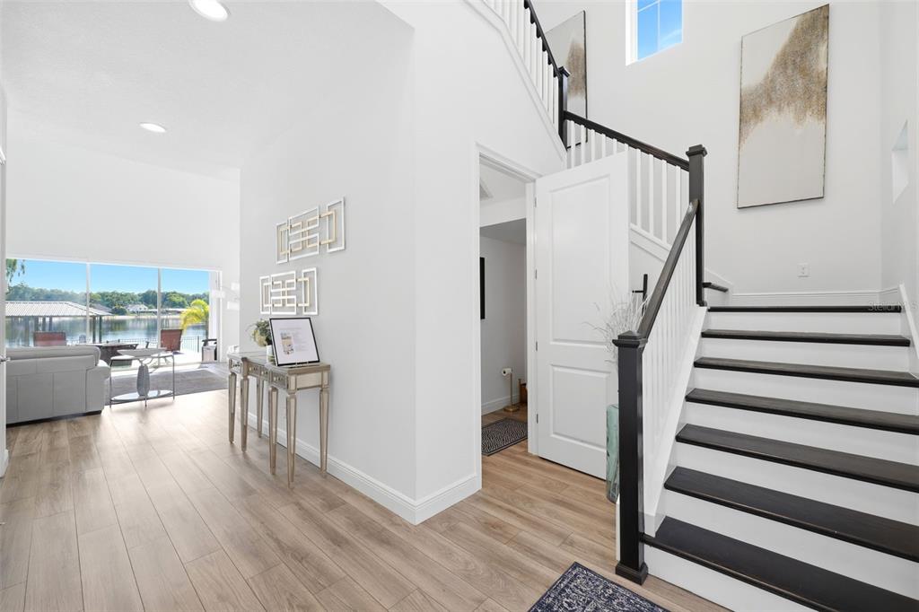 A bright foyer features light wood floors, a staircase with dark treads, and a lake view — 17104 CRAWLEY ROAD, ODESSA, FL