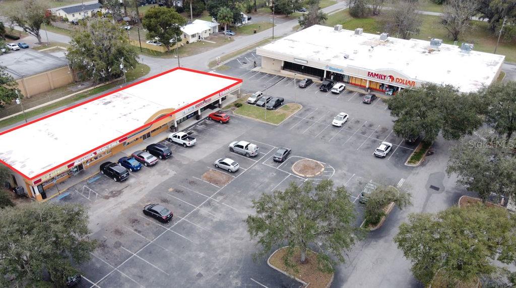 An aerial view shows two commercial strip mall buildings with parking lots and surrounding trees — 5810 SE ABSHIER BOULEVARD, BELLEVIEW, FL