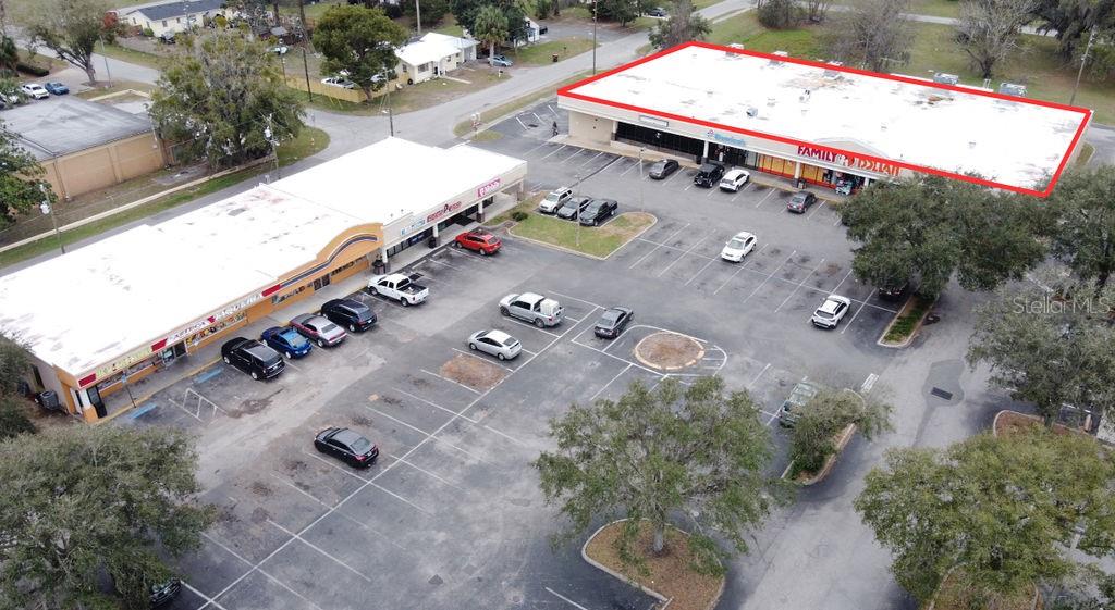 An aerial view shows two commercial strip mall buildings with parking lots and surrounding trees — 5810 SE ABSHIER BOULEVARD, BELLEVIEW, FL