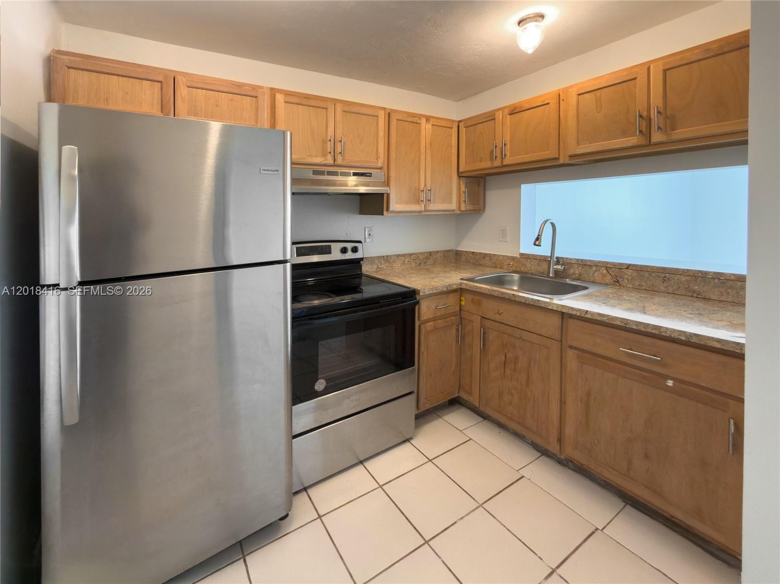 A kitchen features wood cabinets, stainless steel appliances, granite countertops, and white tile flooring — 496 NW 165th St Rd # 410, Miami FL 33169, MIAMI, FL