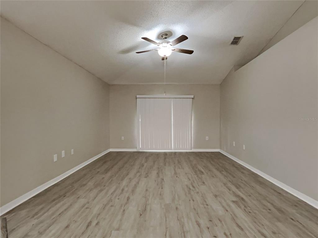An empty room features light-colored wood-look flooring, beige walls, a ceiling fan, and sliding doors — 508 CLOUDCROFT DRIVE, DELTONA, FL