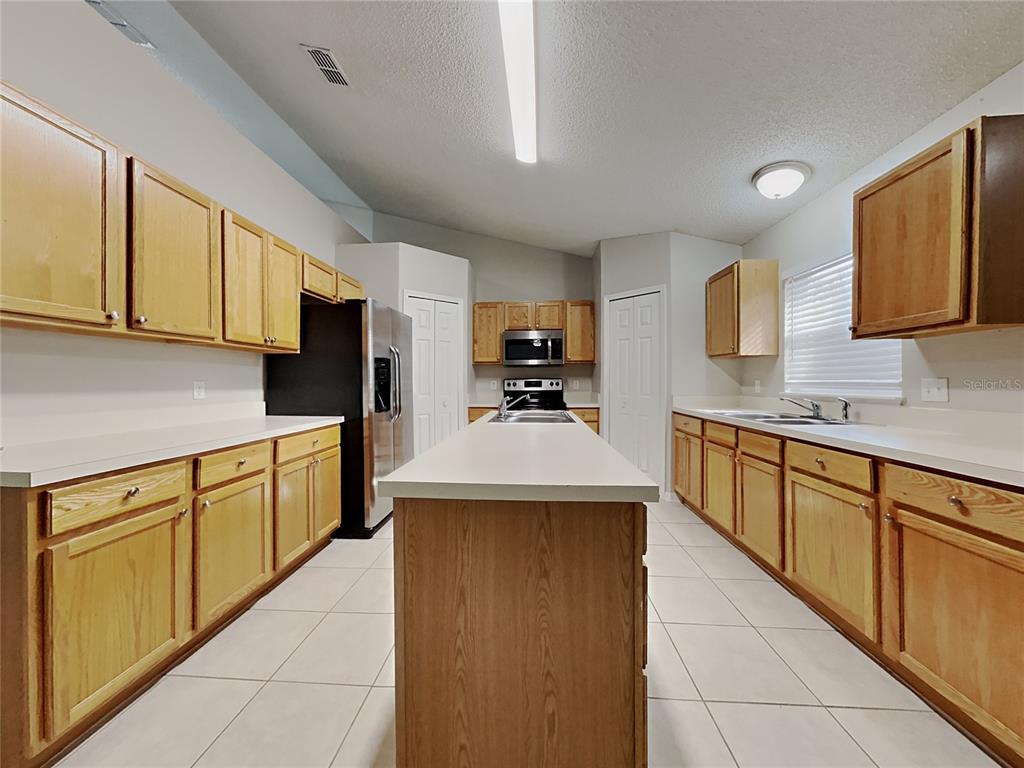 A kitchen features light wood cabinets, white countertops, a central island, and tile flooring — 508 CLOUDCROFT DRIVE, DELTONA, FL