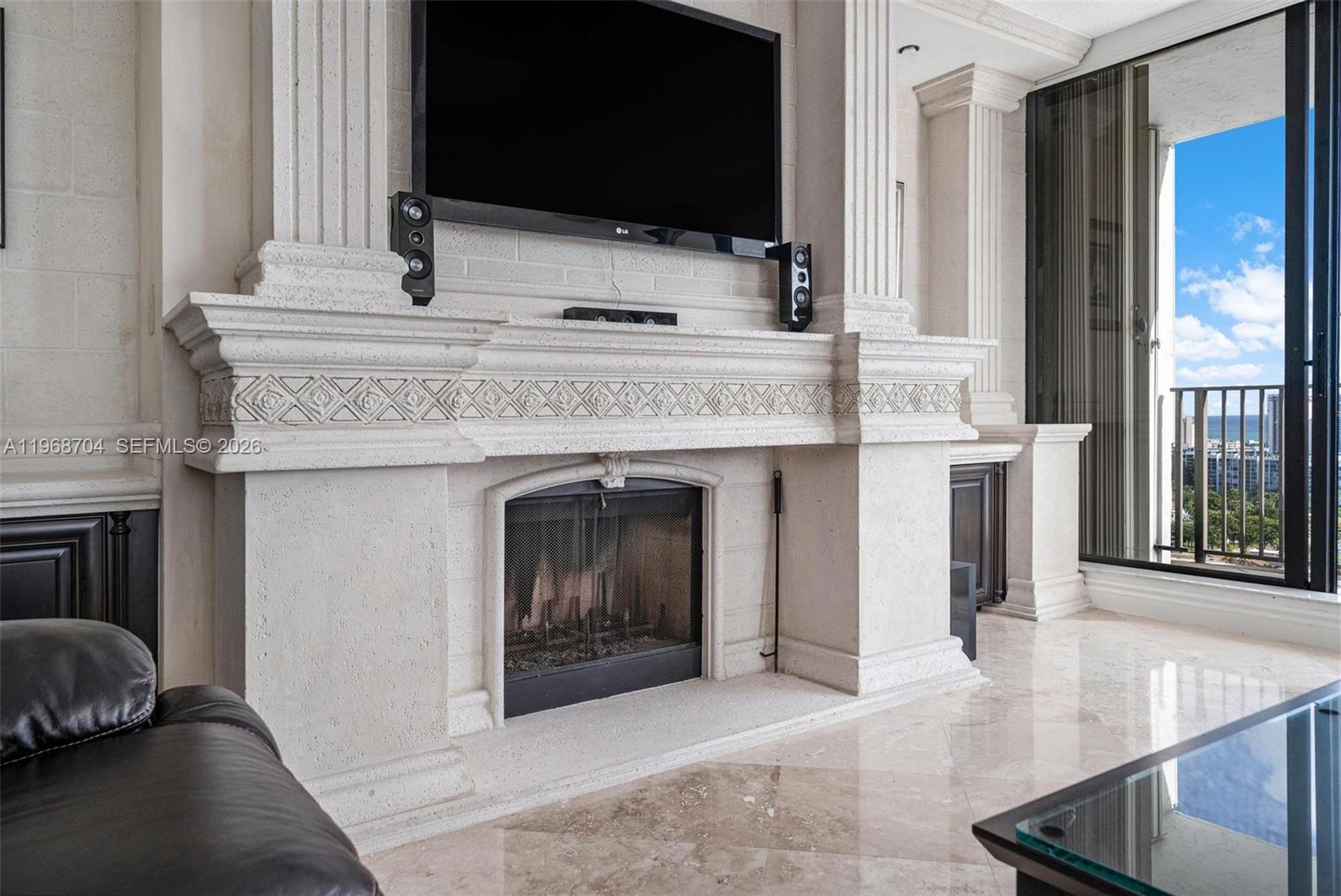A living room features a stone fireplace, a wall-mounted television, and a balcony with ocean views — 300 Three Islands Blvd, Hallandale Beach FL 33009, HALLANDALE BEACH, FL