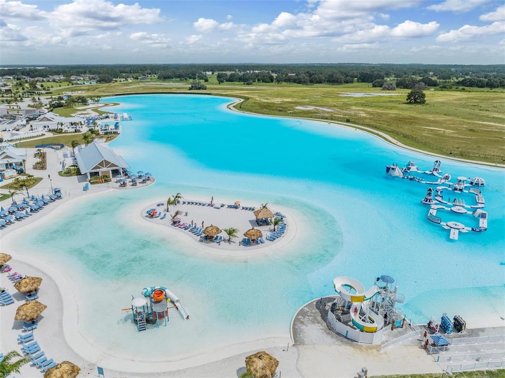 An aerial view shows a large turquoise lagoon with a central island and water slides — 10412 FIELDSTONE MYRTLE WAY, SAN ANTONIO, FL