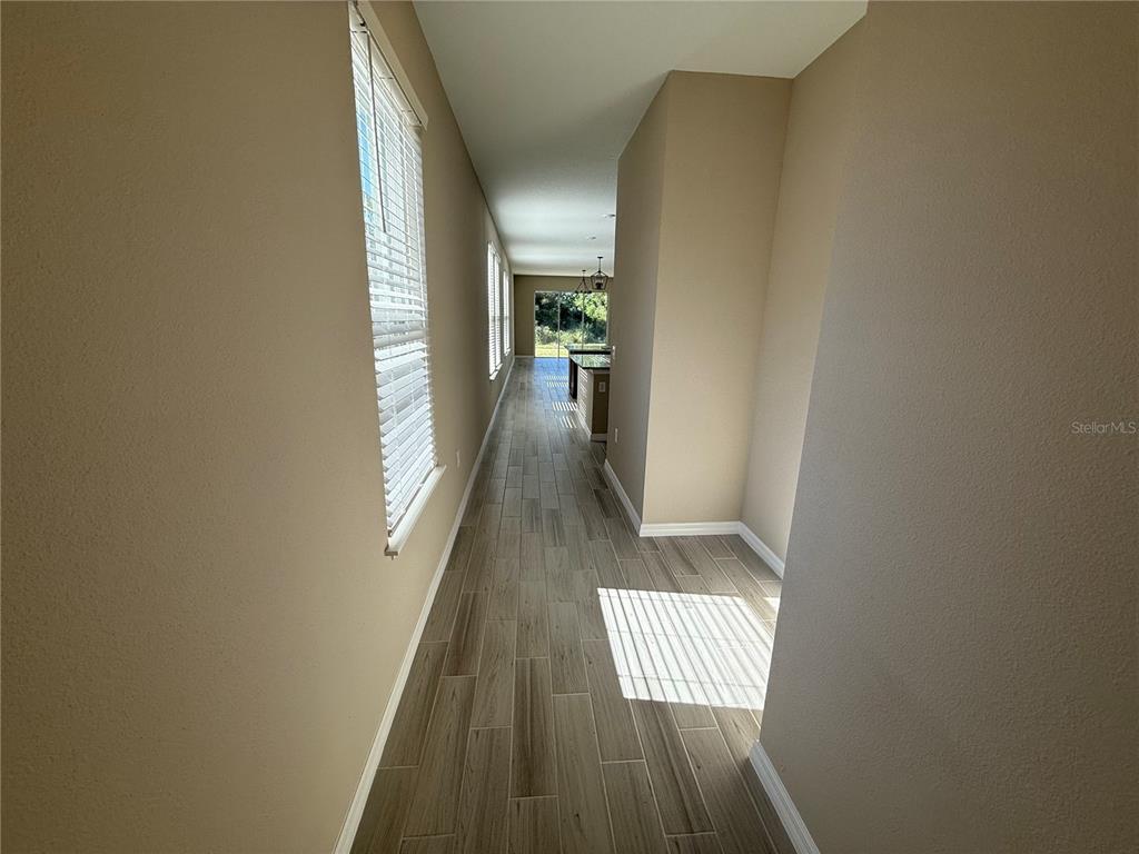 A long hallway with wood-look tile flooring leads toward an open kitchen and backyard view — 15013 SHADY PALMS LANE, NOKOMIS, FL