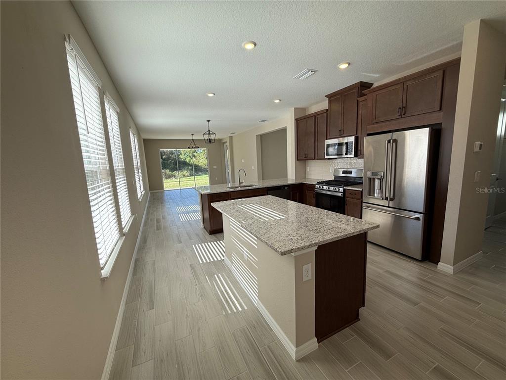 A kitchen features a granite-topped island, dark wood cabinetry, stainless steel appliances, and tile flooring — 15013 SHADY PALMS LANE, NOKOMIS, FL