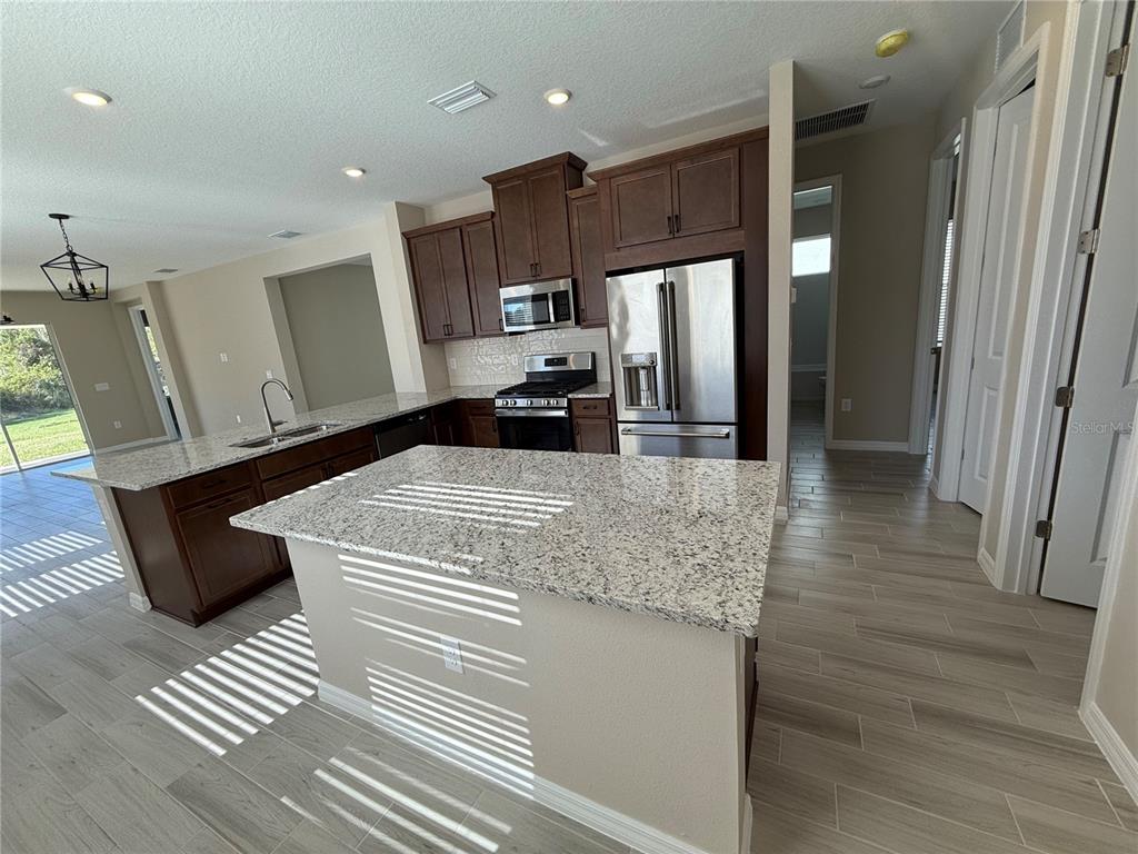 A kitchen features dark wood cabinets, granite countertops, a center island, and stainless steel appliances — 15013 SHADY PALMS LANE, NOKOMIS, FL