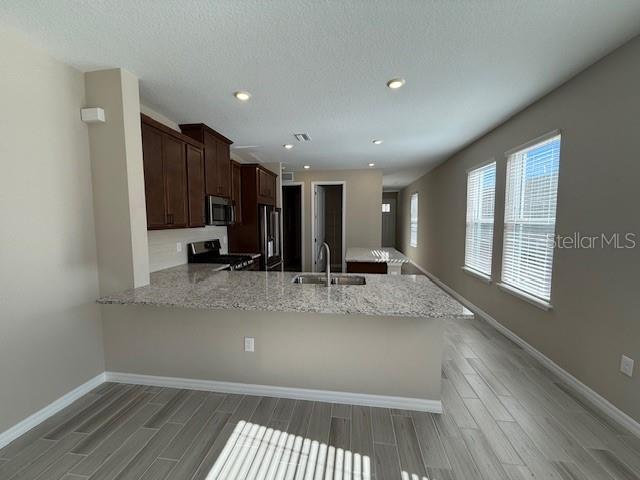 A kitchen features dark wood cabinets, granite countertops, and light-colored wood-look tile flooring — 15013 SHADY PALMS LANE, NOKOMIS, FL