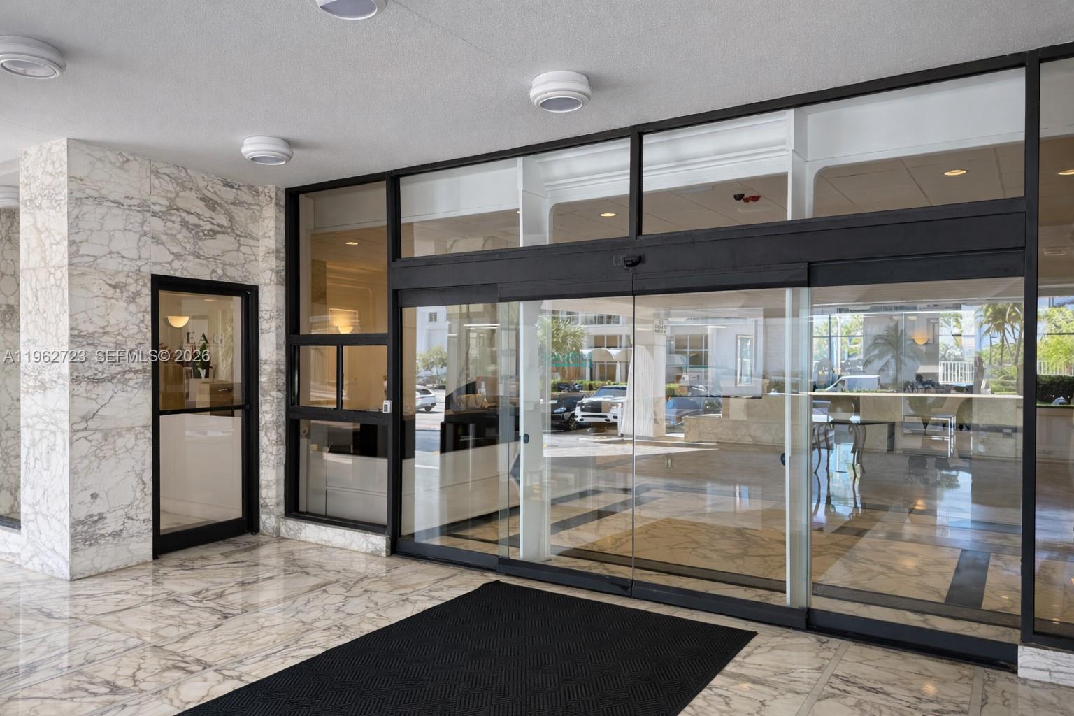 A marble-floored building entrance features glass sliding doors and a black floor mat — 5700 Collins Ave # 1, Miami Beach FL 33140, MIAMI BEACH, FL