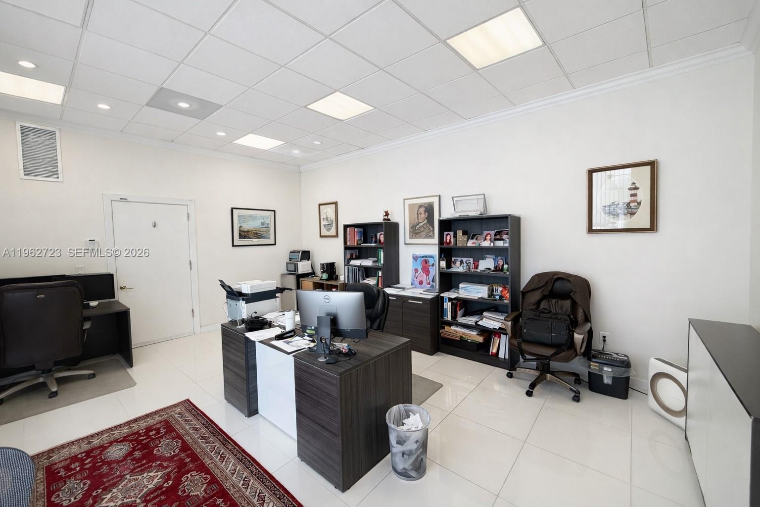 An office space features two desks, dark shelving units, a red rug, and white tile flooring — 5700 Collins Ave # 1, Miami Beach FL 33140, MIAMI BEACH, FL