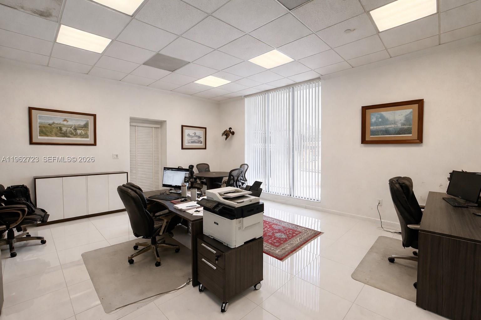 An office space features white tile floors, drop ceilings, two desks, and framed wall art — 5700 Collins Ave # 1, Miami Beach FL 33140, MIAMI BEACH, FL