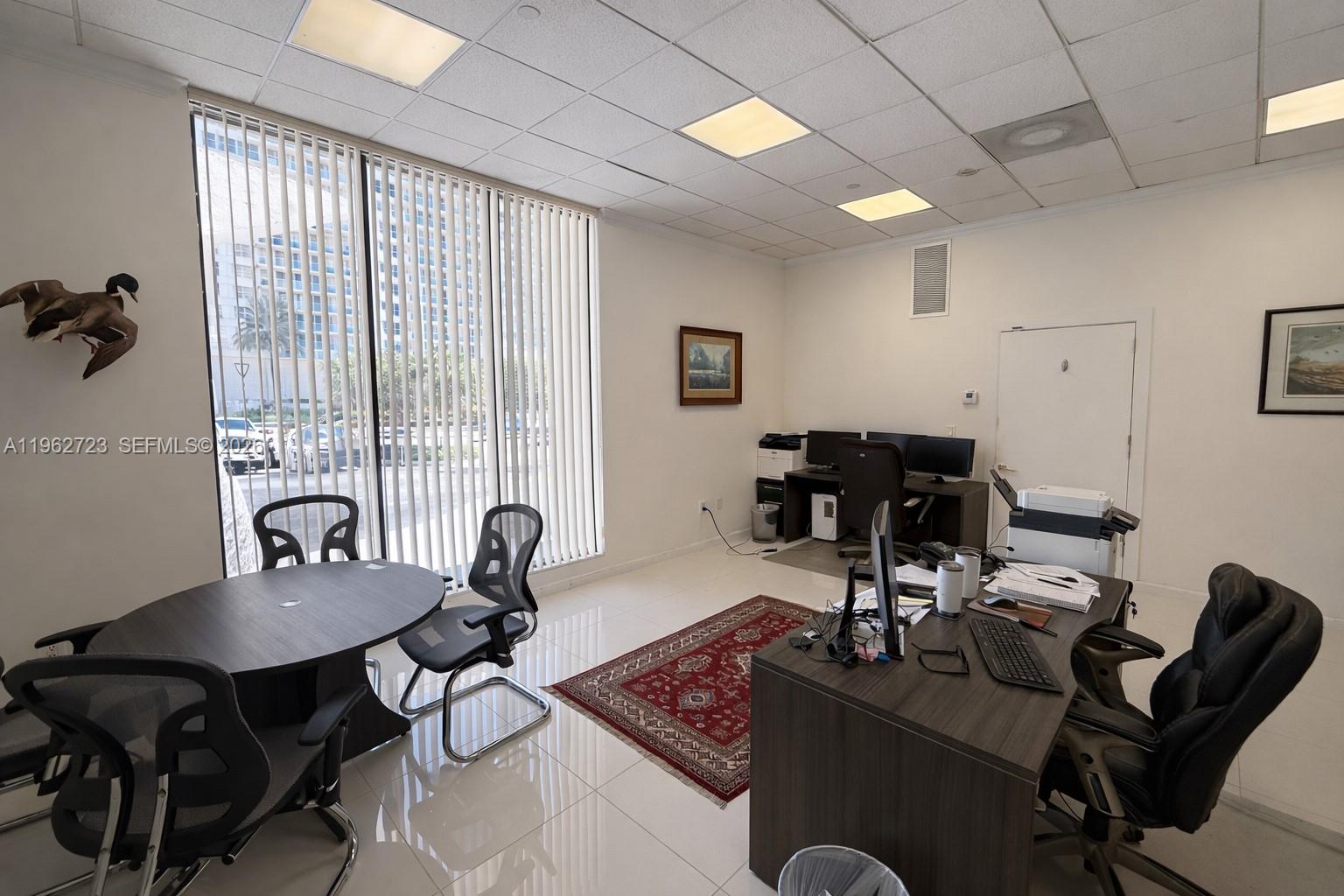 An office features a desk, a conference table, tiled floors, and vertical window blinds — 5700 Collins Ave # 1, Miami Beach FL 33140, MIAMI BEACH, FL
