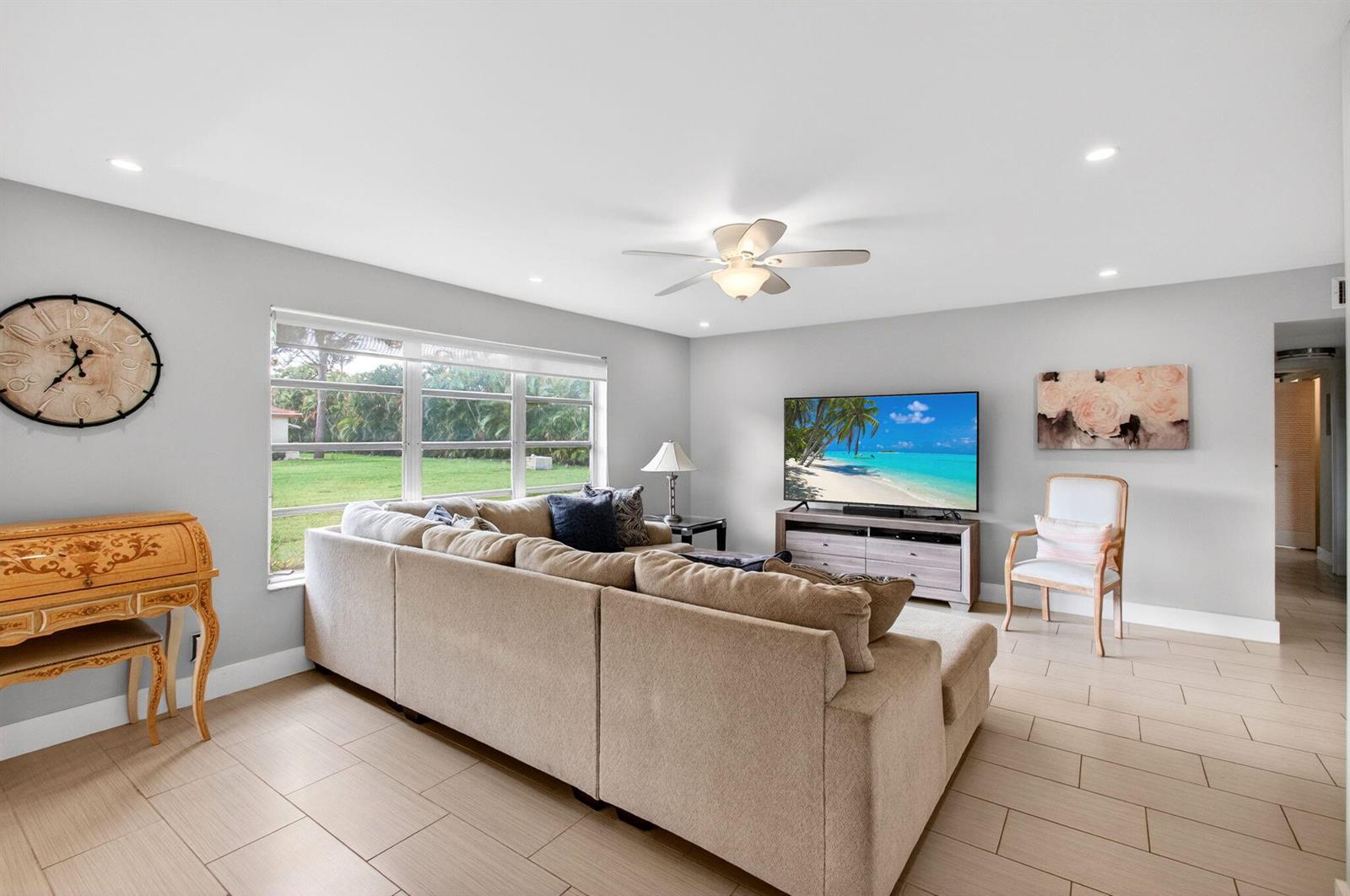 A living room features a beige sectional sofa, a television, and light-colored tile flooring — 5250 NW 3rd Court # A, Delray Beach FL 33445, DELRAY BEACH, FL
