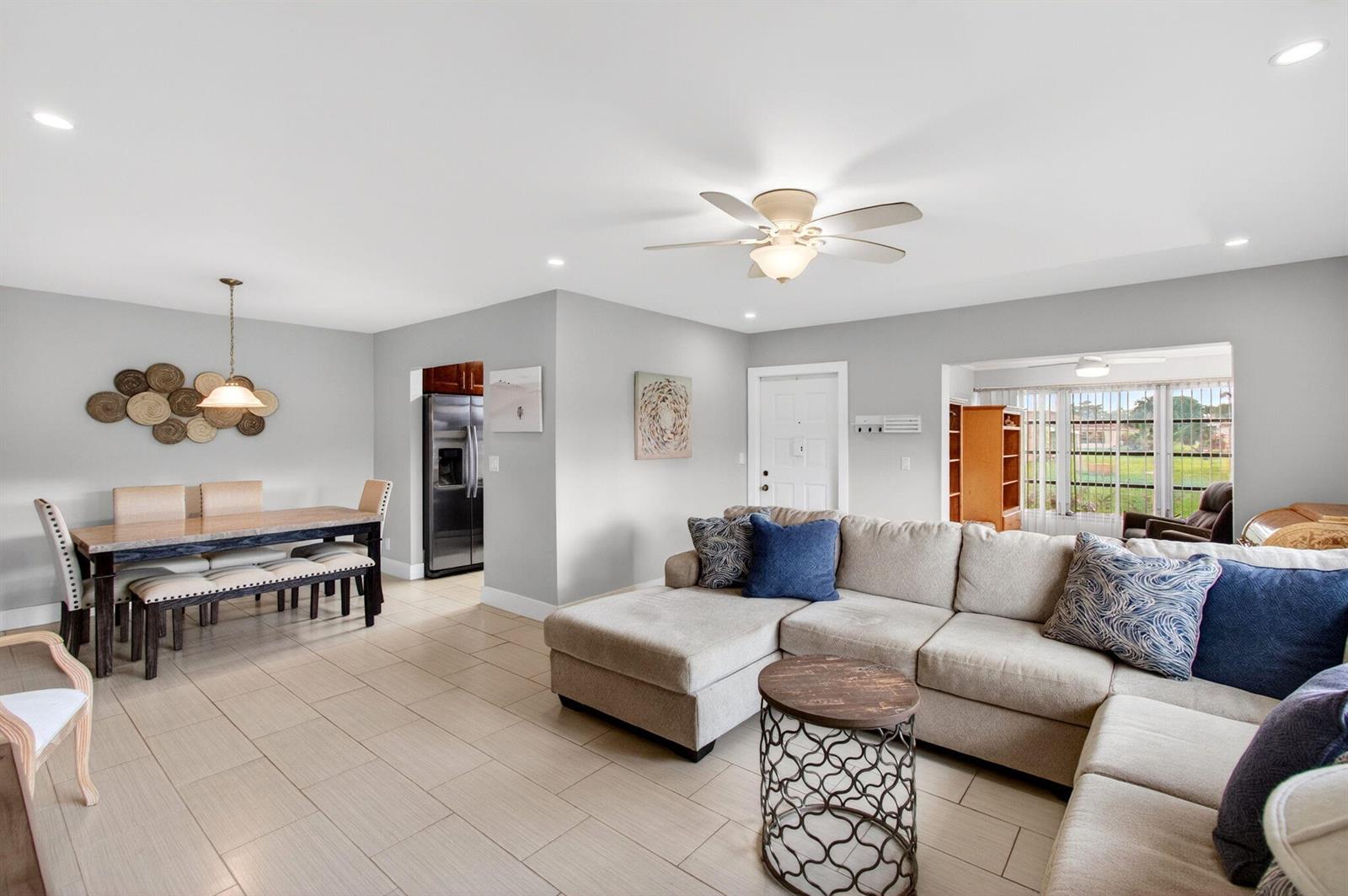 An open-concept living and dining area features light tile flooring, a sectional sofa, and furniture — 5250 NW 3rd Court # A, Delray Beach FL 33445, DELRAY BEACH, FL