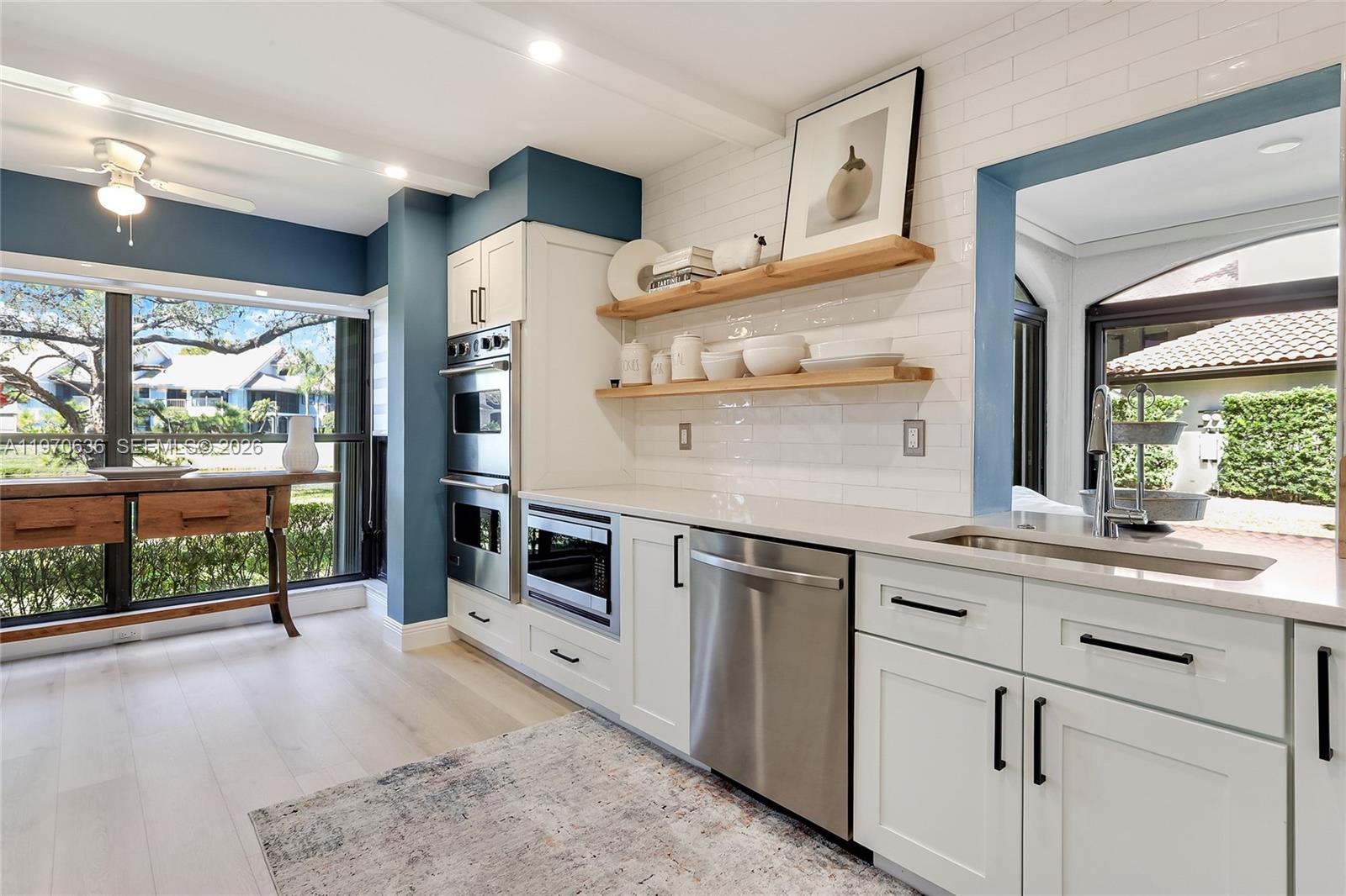 A modern kitchen features white cabinets, stainless steel appliances, open wood shelving, and blue walls — 16671 N Traders Crossing N # 121, Jupiter FL 33477, JUPITER, FL