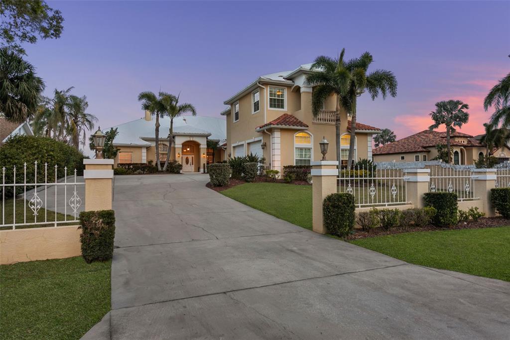 A two-story stucco house with a concrete driveway and white metal fencing at dusk — 4915 TROYDALE ROAD, TAMPA, FL