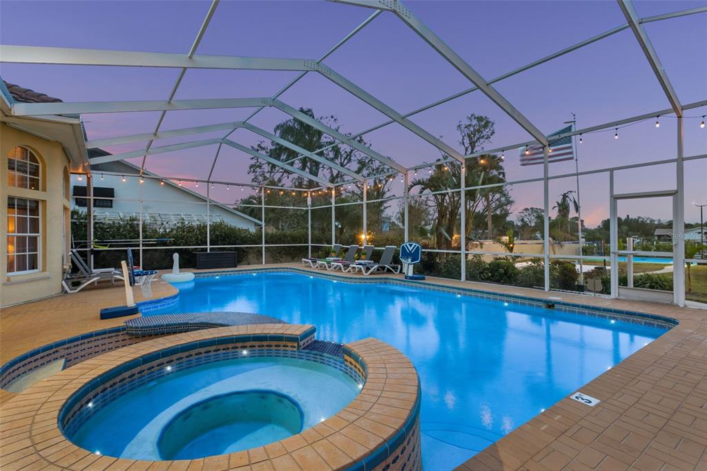A screened-in swimming pool and hot tub are located on a paved patio at dusk — 4915 TROYDALE ROAD, TAMPA, FL