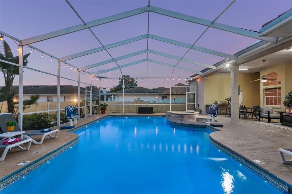 A swimming pool and hot tub are enclosed within a screened lanai at dusk — 4915 TROYDALE ROAD, TAMPA, FL